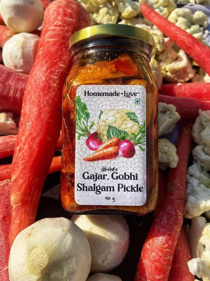 Our Gajar Gobhi Shalgam pickle jar surrounded by the fresh ingredients that go into it. We use juicy carrots, crisp cauliflower, and tender turnips to create this winter delicacy.