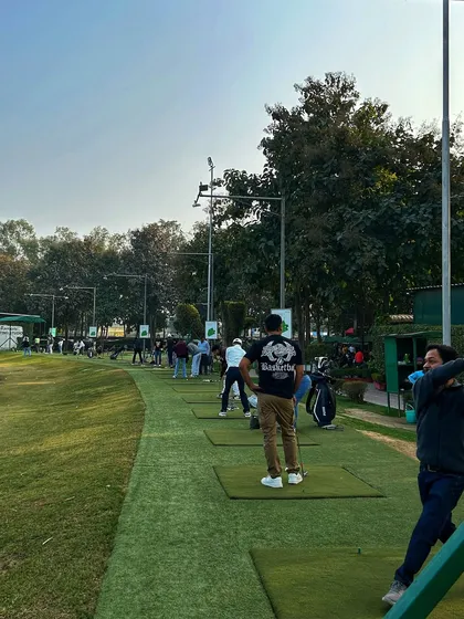 A full driving range on a hazy afternoon, with golfers of all ages enjoying the facility.