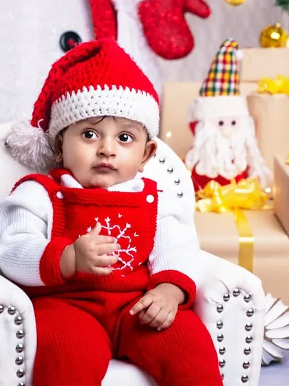 A sweet baby boy in a red snowflake sweater, looking thoughtful as he sits in his chair, surrounded by the festive Christmas decor.