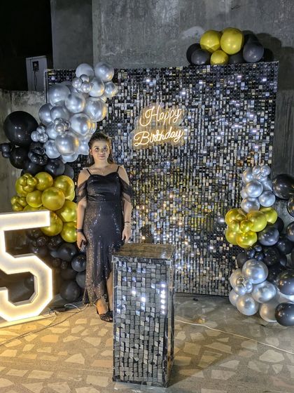 A client stands proudly next to her glamorous birthday setup, featuring a sequin wall and a large '15' marquee number.