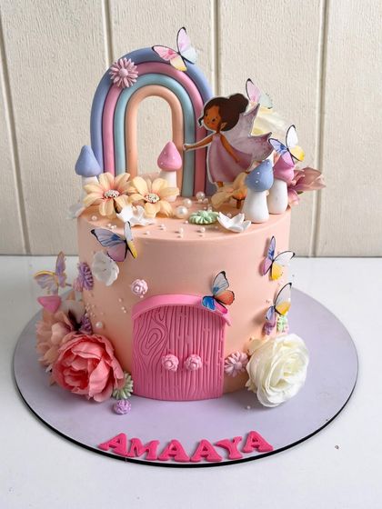 A whimsical fairy-themed cake in soft peach tones. This design includes a pastel rainbow arch, delicate butterflies, hand-sculpted mushrooms, and fresh flowers, creating an enchanting garden scene for a magical birthday.