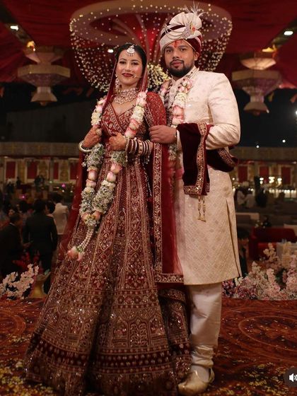 A full-length shot of the beautiful couple. The bride's maroon lehenga is intricately detailed, and her makeup is designed to be elegant and timeless for this once-in-a-lifetime moment.