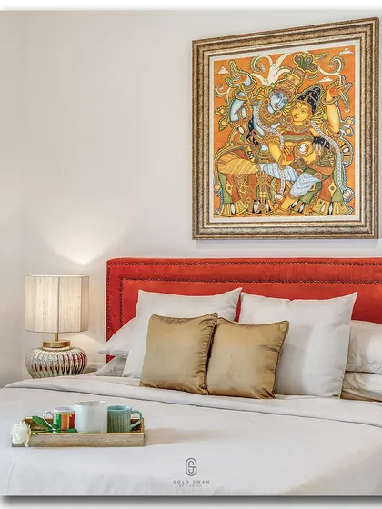 A close-up of a bedroom that blends traditional art with contemporary comfort. A vibrant, traditional Indian painting hangs above a bright red headboard, creating a striking focal point in this elegantly styled room.
