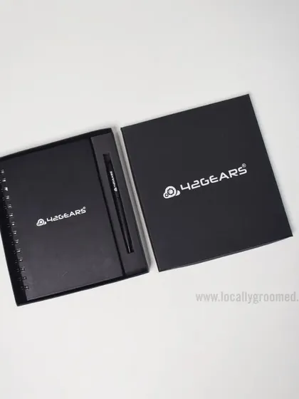 A classic and professional gift set for 42Gears. This includes a black spiral notebook and a matching pen, presented in a sleek box with the company's logo prominently displayed.