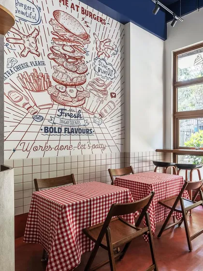 We brought a burger brand's playful personality to life with a custom, large-scale wall mural that serves as the centerpiece of the diner. Paired with classic red-and-white gingham tablecloths and simple wooden chairs, the design creates a fresh, modern take on retro American diner aesthetics.