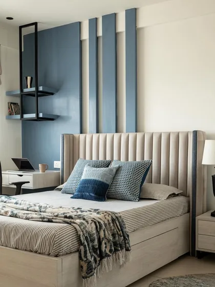 The master bedroom was designed as a serene retreat with a functional workspace. The blue accent wall with vertical panels adds height and interest, while the upholstered headboard provides a soft, comfortable backdrop.