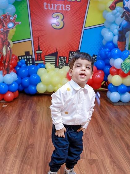 The birthday boy stands proudly in front of his personalized superhero backdrop. We customize our decor to feature your child's name and age, making them the star of the show.