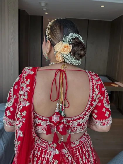 The final look of the peach rose and baby's breath bun, paired with a red lehenga. The back view shows the neatness of the bun and the beautiful contrast of the flowers.