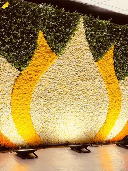 A magnificent floral wall featuring a large lotus motif created with orange, yellow, and white flowers against a green leaf base. This backdrop is perfect for a Haldi ceremony or a spiritual event.