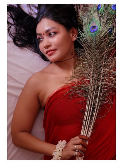 An artistic portrait featuring a peacock feather. The composition and the subject's expression create a sense of connection to nature and a quiet, meditative mood.