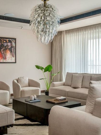 The formal living room at the Parishram residence is designed for sophisticated entertaining. A statement glass chandelier hangs above a serene, monochromatic seating arrangement, creating an atmosphere of quiet luxury.