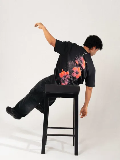 A dynamic, off-balance pose on a stool. This creative shot showcases the floral graphic on the back of the t-shirt while creating a visually interesting and artistic image.
