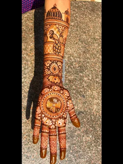 A beautiful bridal mehendi design on a practice hand, showcasing a peacock and palace theme.