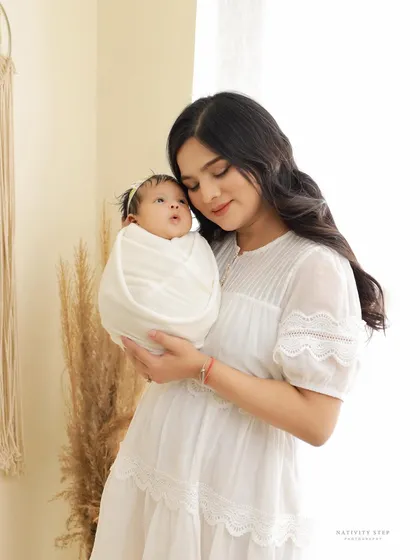 A mother gazes lovingly at her newborn, who is swaddled in pure white. The bright, airy setting with natural light creates a soft and angelic mood for this mother-child portrait.
