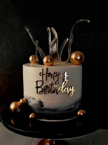 A modern cake with a dramatic black background, topped with a clear pulled sugar splash and gold spheres. This design is artistic, elegant, and perfect for a stylish celebration.