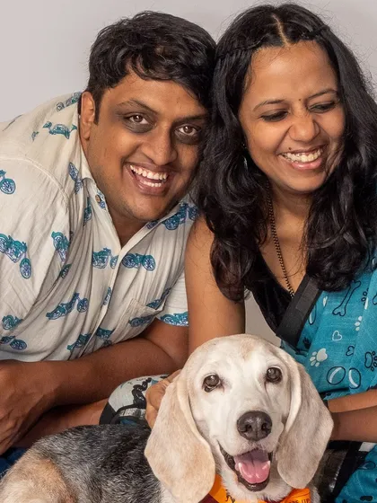 A happy family portrait of Kavitha and Rishi with their beagle, Seenu. Their bright smiles show the love and joy their adopted dog brings them.