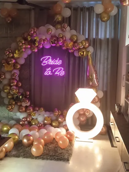 This indoor 'Bride to Be' setup combines a circular balloon arch with a large, light-up diamond ring prop. The rose gold, white, and chrome balloons create a chic and celebratory look for the party.