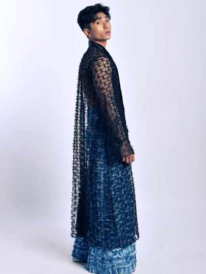 A dramatic full-length shot. The long, sheer coat adds a sense of movement and theatricality to the entire outfit.