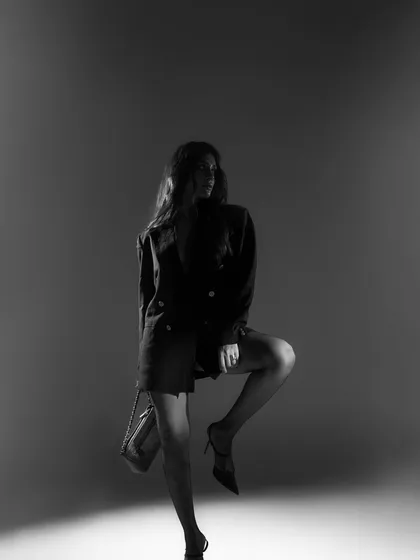 A full-length black and white shot that plays with silhouette and shadow. The model's dynamic pose and the focused spotlight create a theatrical and artistic image.