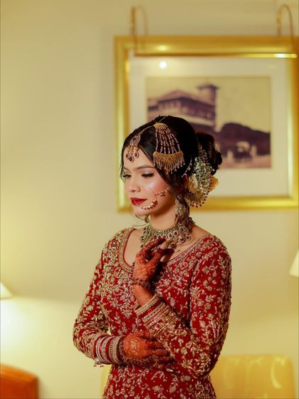 A beautiful portrait of the bride, highlighting her soft glam makeup and intricate hairstyle. The red outfit and gold jewelry complete this classic Nikkah look.