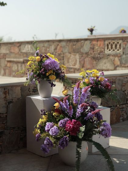 More floral details from the Haldi, with arrangements placed on white plinths against the rustic stone wall of the venue.