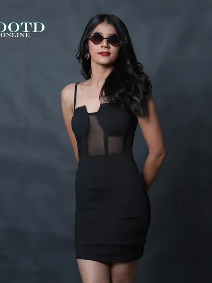 A cool and chic studio shot for a brand, featuring a model in a black corset dress and sunglasses against a dark background.