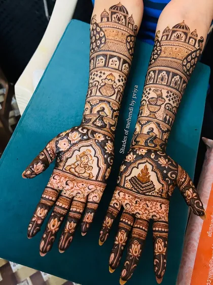 This intricate bridal mehendi showcases a variety of traditional wedding elements. One hand features a Ganesha figure for blessings, while the other has a sacred fire (havan kund), with wedding ritual scenes filling the arms.