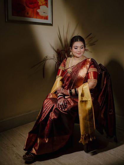A serene portrait of the bride seated, her magnificent maroon and gold saree draped elegantly around her.