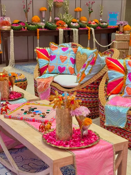 An overview of the lounge seating at our vibrant Garba celebration. The area is filled with colorful cushions, traditional wicker furniture, and tables adorned with flower petals and nostalgic games.