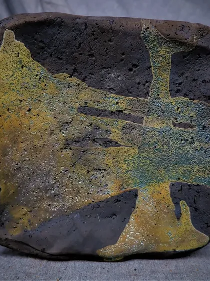 An abstract, textured tile after Raku firing. The volcanic, earthy texture and colors are a perfect example of what makes this technique so special.