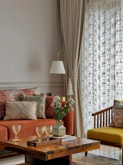 This living room balances a simple, earthy terracotta sofa with vibrant patterned cushions. A bright yellow accent chair and sheer curtains complete the warm, inviting, and light-filled space.