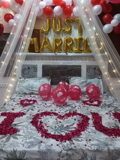 A classic 'Just Married' room decoration to welcome the newlyweds. I used a canopy with fairy lights, 'Just Married' foil balloons, and a heart shape made of rose petals on the bed for a truly romantic atmosphere.