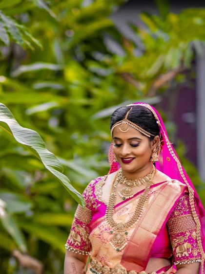 A close-up of the bride, her face framed by a leaf. The soft colors of her saree and the intricate embroidery on her blouse are highlighted.