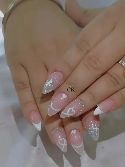 A romantic and delicate set featuring a white French tip, hand-painted white hearts and ribbons, and sparkling accent nails.