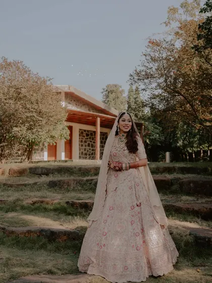 A stunning full-length bridal portrait in the gardens of the wedding venue. The bride's elegant lehenga and happy expression are the focus of this beautiful shot.