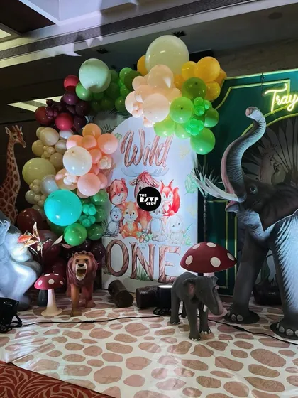 Time for a wild adventure! This 'Wild One' first birthday backdrop features adorable illustrated animals, life-size props of an elephant and lion, and a lush balloon garland to create a picture-perfect jungle safari scene.