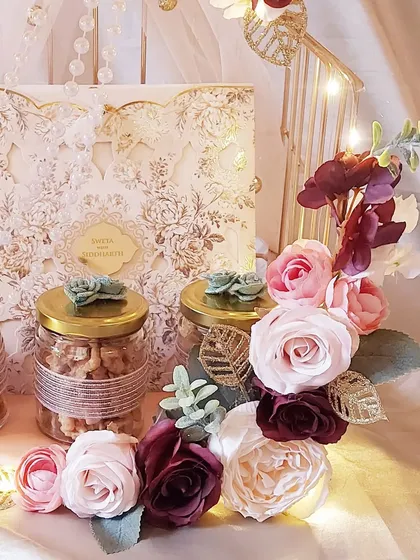 A closer look at the details of our floral wedding invitation hamper. The intricate laser-cut card is the star, complemented by jars of nuts and elegant floral arrangements, all lit by our signature fairy lights.