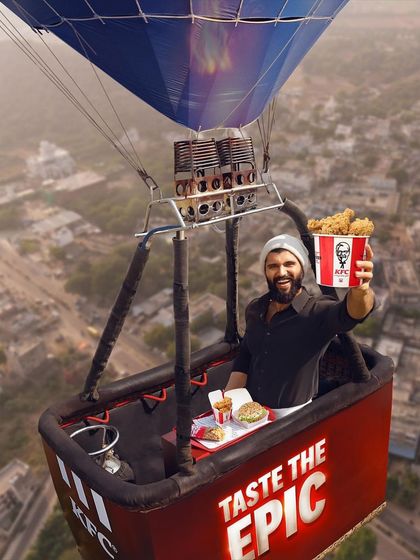 The hero shot from the KFC hot air balloon campaign. Vijay Deverakonda's look is understated, allowing the grand scale of the scene and the "Taste the Epic" branding to take center stage.
