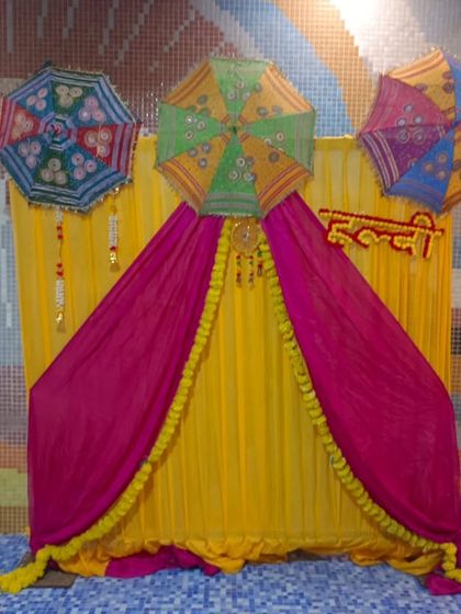 A poolside Haldi setup with a backdrop of yellow and pink drapes, decorated with Rajasthani umbrellas. The colorful mosaic tiles of the pool area complement the festive decor.