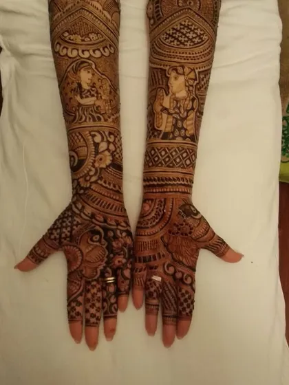A full-arm bridal design featuring portraits of the bride on the forearms, surrounded by peacocks and intricate traditional patterns.