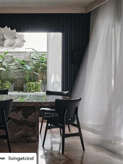 The dining room, where sheer curtains billow in the breeze, softening the dramatic, dark features of the space. The view into the green courtyard adds a sense of tranquility.
