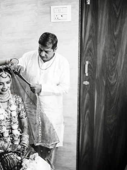 A black and white documentary shot of the family helping the bride with her veil, while another family member looks on.