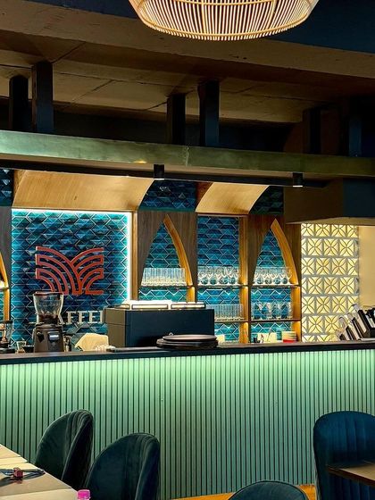 A view of our beautifully designed bar area, with its intricate turquoise tiling, warm backlighting, and elegant glassware ready for service.