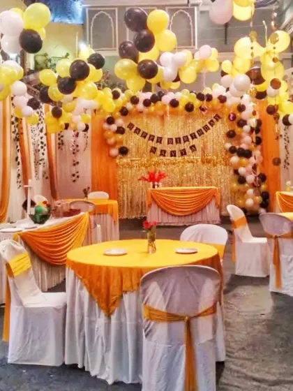 A complete birthday party hall decoration with a yellow, black, and white theme. I arranged the guest seating with matching table covers and set up a shimmering gold backdrop with a balloon arch.