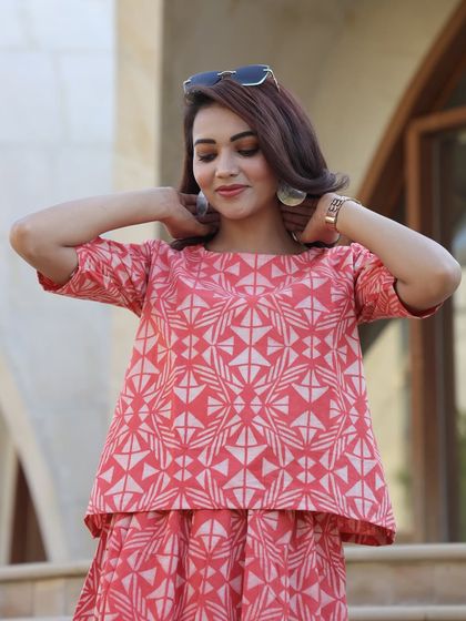 A detailed shot of the coral pink top, highlighting the unique geometric pattern and the quality of the cotton fabric.