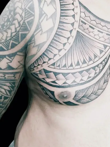 A powerful Polynesian and tribal style tattoo covering the chest and shoulder. This type of work involves creating intricate, flowing patterns that complement the body's natural lines. Each symbol can hold personal meaning, telling a story on the skin.