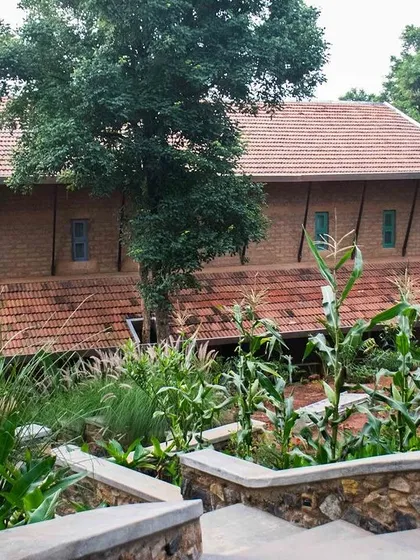A view of the PLENTI House, showing how the different levels of the building are nestled into the hillside. The roofs are tiled in a traditional style, and the walls are made of sun-dried adobe bricks.