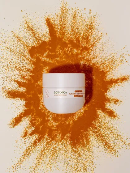 A creative shot of a turmeric face mask with a splash of turmeric powder. The dynamic "explosion" of powder adds energy and visual interest to a standard product shot.