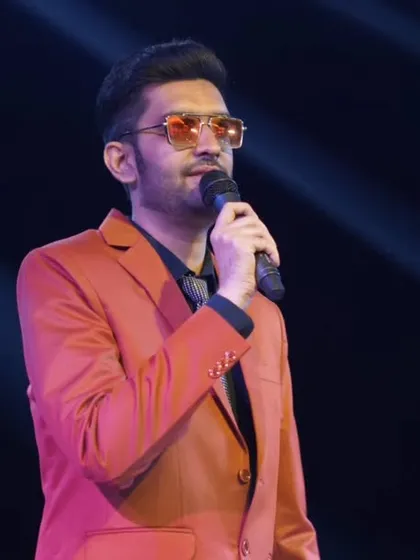 A close-up shot on stage in a sharp orange suit. Every word and gesture is meant to weave a story of celebration.
