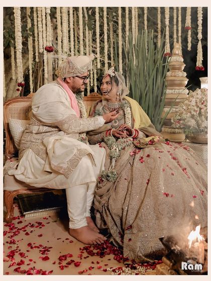 A candid moment during the wedding ceremony, with the couple sharing a laugh while seated at the mandap, surrounded by fire and flower petals.